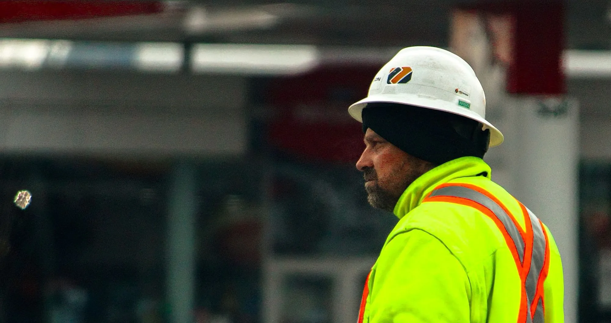 Trois personnes en casque de chantier consultent une tablette sur un site de construction.