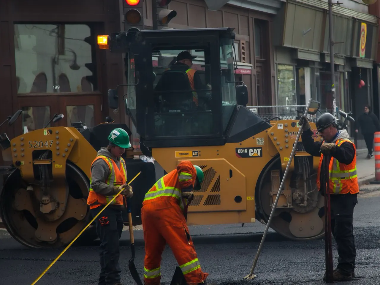 Équipe de voirie en dossards orange posant de l'asphalte derrière un rouleau compresseur dans une rue de la ville de Québec.