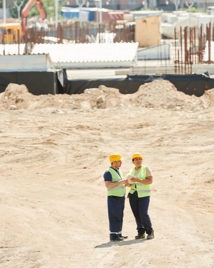 Deux travailleurs en dossards de sécurité discutant au milieu d'un chantier d'excavation.