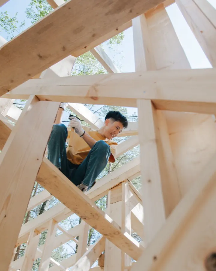 Travailleur de la construction assemblant une charpente de bois en hauteur sur un chantier ensoleillé.