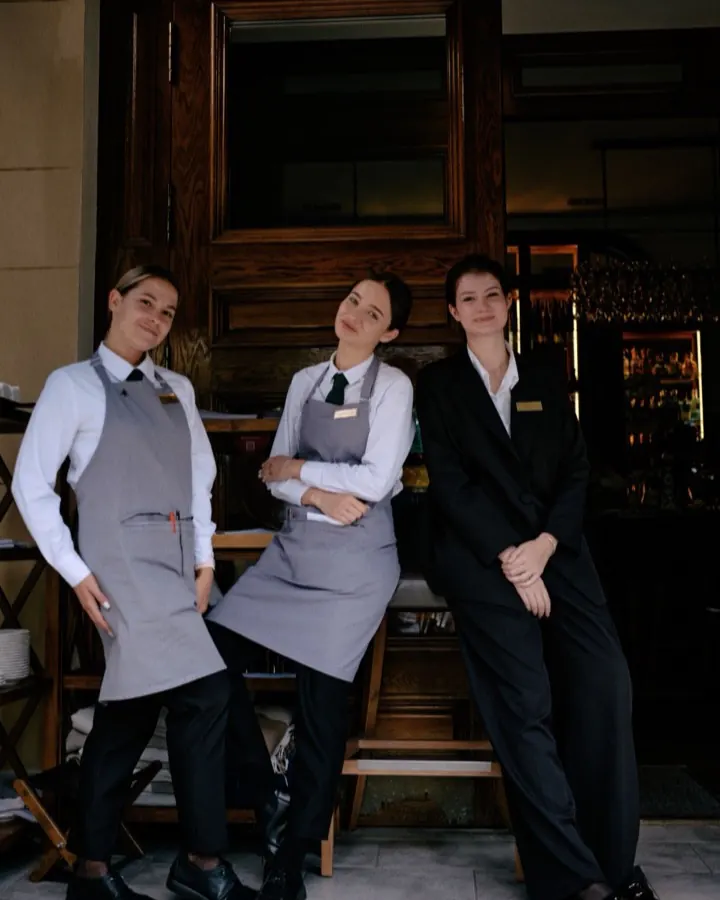 Trois membres du personnel d'un restaurant, en uniforme, devant l'entrée de l'établissement.